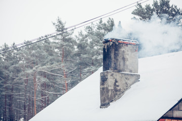 Old snow covered roof with smoke chimney in rural Latvia, Europe .Black weathered with texture. Trees in background.