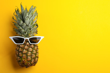 Pineapple with sunglasses on yellow background, top view. Space for text