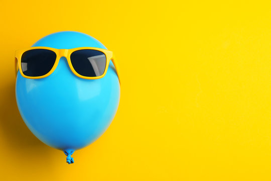 Balloon with sunglasses on yellow background, top view. Space for text