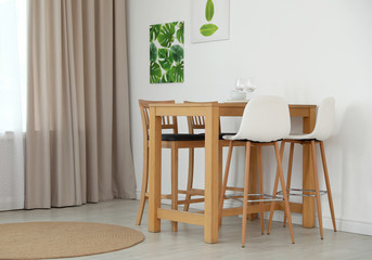Stylish room interior with dining table and bar stools near white wall
