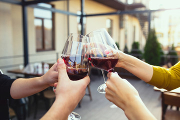 People clinking glasses with wine on the summer terrace of cafe or restaurant. Happy cheerful friends celebrate summer or autumn fest. Close up shot of human hands, lifestyle.