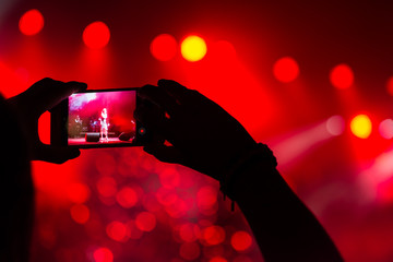 At a music festival, a man records his concert on his smartphone. Hands silhouette, soft focus
