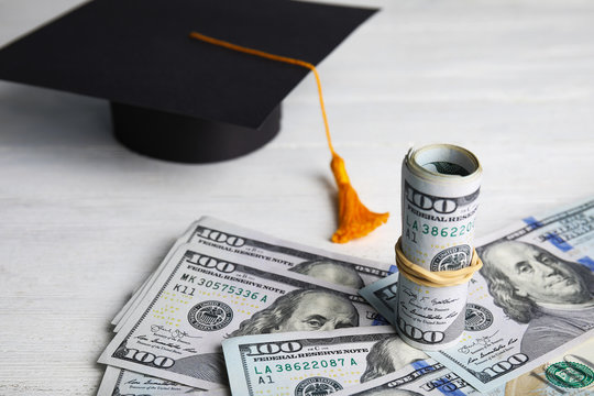 Dollar banknotes and student graduation hat on white wooden background. Tuition fees concept