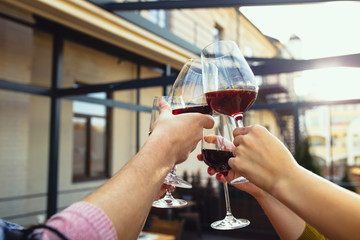 People clinking glasses with wine on the summer terrace of cafe or restaurant. Happy cheerful friends celebrate summer or autumn fest. Close up shot of human hands, lifestyle.