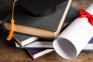 Graduation hat, books and student's diploma on wooden table, closeup