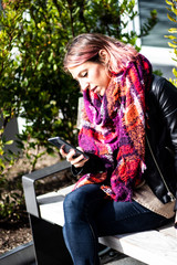 Portrait of a beautiful young female student sitting outside reading her text messages on her cell...