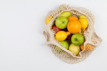Mesh shopping bag with fruits apples, oranges, lemon and pears on white background.