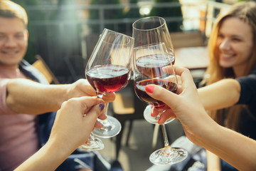 People clinking glasses with wine on the summer terrace of cafe or restaurant. Happy cheerful friends celebrate summer or autumn fest. Close up shot of human hands, lifestyle.