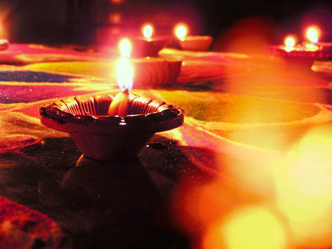 low angle shot of diwali oil clay lamps with intricate red green colored design placed on multicoloured rangoli background