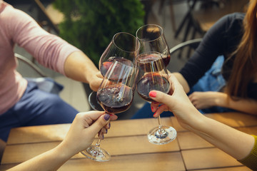 People clinking glasses with wine on the summer terrace of cafe or restaurant. Happy cheerful friends celebrate summer or autumn fest. Close up shot of human hands, lifestyle.