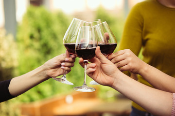 People clinking glasses with wine on the summer terrace of cafe or restaurant. Happy cheerful friends celebrate summer or autumn fest. Close up shot of human hands, lifestyle.
