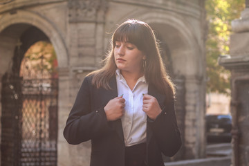 Fototapeta premium Business lady with dark brown hair. Stylish girl. Fashion.White shirt, black jacket, black skirt. Background of old building.