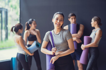 Fototapeta na wymiar Asian cute woung girl stand in the front Group of mix race of Caucasian and Asian sporty people both women and men talk and Laugh at black wall waiting for enjoy yoga class together