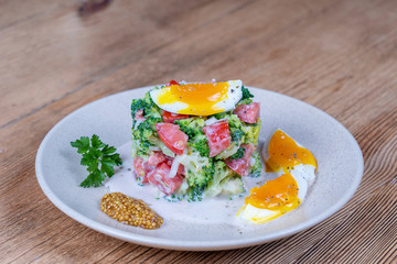 Delicious salad with broccoli, tomato, onion and boiled egg with cream sauce in plate on wooden background. Healthy food