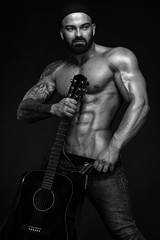 Strong and fit man bodybuilder with guitrar shows abdominal muscles. Sporty muscular guy athlete....