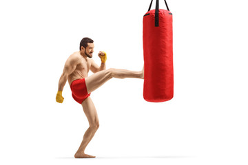 Young muscular man exercising kickboxing and kicking a punching bag with his leg