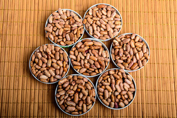 Seven bowls with organic fresh red beans on a wooden table displayed as a flower in warm light, top view
