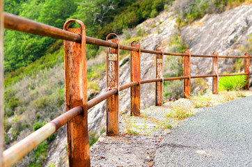 Fototapeta na wymiar Old rusty metal fence on the road in the mountains