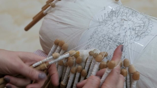 Lady's hands, making bobbin lace, weaving the bobbins. A woman weaves lace in the old fashion. Handwork. Close-up.