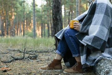 Woman with plaid and cup of hot drink in pine forest, space for text