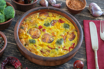 Ceramic bowl with vegetable frittata, simple vegetarian food. Frittata with egg, tomato, pepper, onion, broccoli and cheese on wooden table. Italian egg omelette