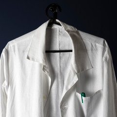 Closeup of a doctor's white lab coat on a hanger against a dark background.