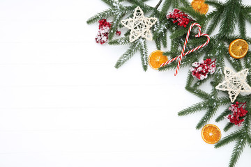 Christmas tree branches with red berries, candies and orange fruit on white wooden table