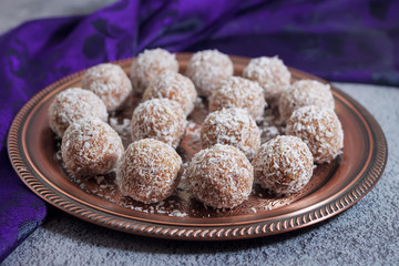 Raw coconut energy balls on a copper oriental plate. Violet silk oriental fabric in the background.