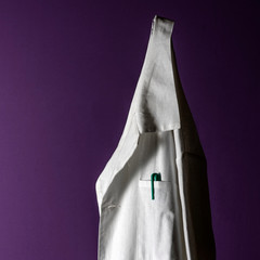 Closeup of a doctor's white lab coat on a hanger against a dark background.