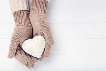 Hands in knitted mittens holding heart on white wooden table