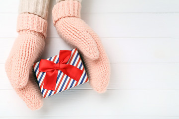 Hands in knitted mittens with gift box on white wooden table
