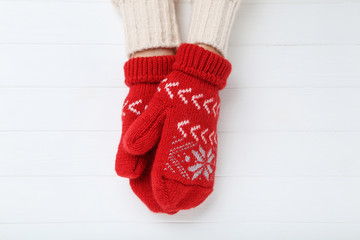 Hands in knitted mittens on white wooden table