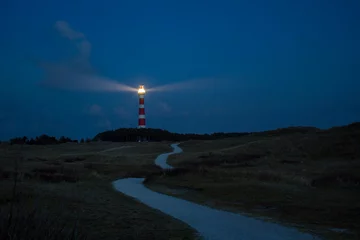 Zelfklevend Fotobehang lighthouse of Ameland at night with light beaming across the deep blue sky © Felix Busse Phtgrphy