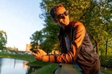 guy and smartphone in the park. in the light of the setting sun in sunglasses