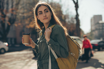 Beautiful woman holding paper coffee cup and enjoying walk in the city