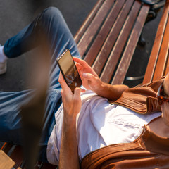 the guy is sitting on the bench resting and looking at the smartphone.