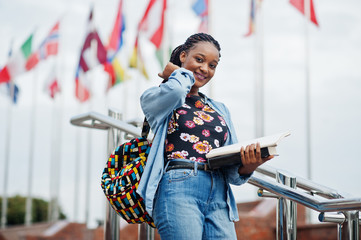 African student female posed with backpack and school items on yard of university, against flags of different countries.