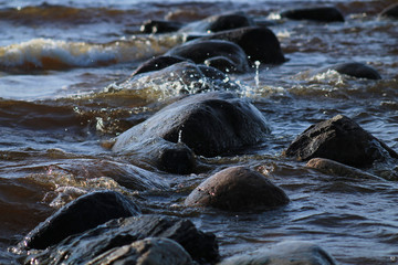 Stones under the sea waves with frozen spray. Focus in the center, blur in the background.