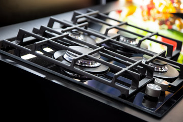 New modern gas stove with four burners for the kitchen, stainless steel surface. Cast iron grates. yellow background in blur