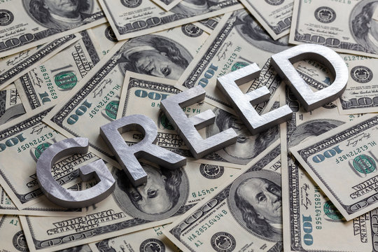 The word GREED laid with aluminium letters on the US dollar banknotes background - with selective focus