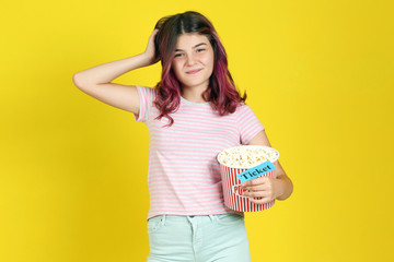 Young girl holding bucket with popcorn and paper with word Ticket on yellow background