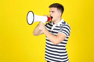 Young man screaming in megaphone on yellow background