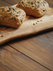 Two sourdough rolls with pumpkin seed on a wooden board and table, Warm brown tones. Bakery product. Close up. Vertical image.