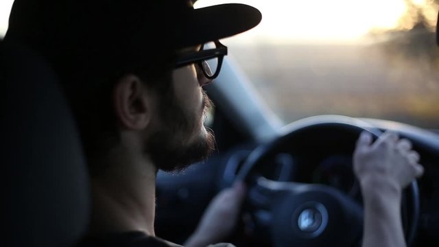 Close-up of young bearded man driving car, with sunlight effect of sunset.