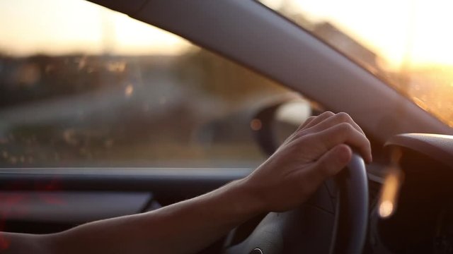 Close-up of male hands on wheel of car driving, background of sunlight effect of sunset.
