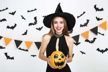 Beautiful woman in black costume holding halloween pumpkin with paper bats and flags on white...
