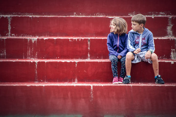 frère et sa soeur assis sur des gradins rouges