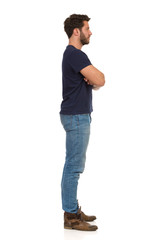 Fototapeta premium Young Man In Jeans And Blue T-shirt Is Standing With Arms Crossed And Looking Away. Side View.