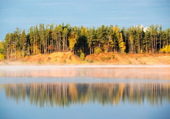 The shore of the misty lake in the early morning lit by the bright sun . Autumn landscape.