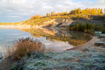 The grass is covered with frost on the shore of the lake early in the morning.